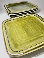 Stacked green ceramic plates showing beaded border detail and glossy glaze finish under lighting.