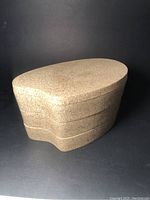 Closed view of the sculptural, speckled beige post modern jewel box with an organic oval shape.