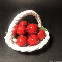 Front angled view showing red glazed cherries in a white twisted ceramic basket with green leaves and wire stems.