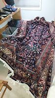Full view of the large traditional style area rug laid out on floor with visible intricate pattern and fringes.