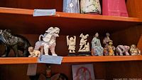 Wide shelf view showing multiple Asian themed figurines including black elephant, foo dog, small human and animal figures, silver elephant, and seated Buddha.