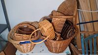 Wide shot showing collection of various sizes and styles of woven wicker baskets stacked on top of each other next to a filing cabinet.