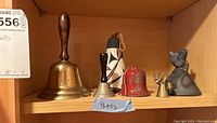Six bells of various sizes and materials on a wooden shelf, showing overall lot contents.