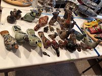 Overview of multiple clay bird figurines of various sizes and colors displayed on a white table, showing range of sizes and detailed hand-painted decorations.