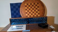 Overview shot showing round wood board, blue square board, metal pieces in display case, small box and Austin brochure