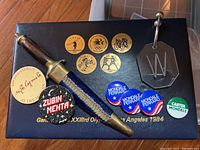 Display of items in the lot on a wooden floor, including coins, pins, decorative dagger, and metal cutter on a black box.