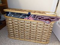 Woven rectangular basket with a hinged lid partially open showing multiple yarn skeins and crocheted fabric pieces inside.