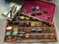 Full collection of cufflinks and tie clips displayed in two trays, showcasing variety of styles and materials.