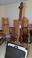 Side view of the vintage wooden artist's easel showing overall structure and some surrounding chairs and furniture in the room.