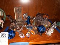 Overview of shelf displaying assorted glass figurines, paperweights, dishes and hourglass timer