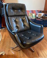 Full view of the black leather tufted Mid-century Modern office chair with surrounding room details.