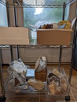 Metal shelving with boxes and containers holding mineral, rock, and geode items arranged inside plastic bins and cardboard boxes