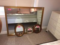 Four framed mirrors including one large rectangular mirror and three smaller oval mirrors shown together leaning against a wall.