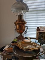 Full view of the metal oil lamp with ribbed glass shade and the assortment of metal pans and trays below it.