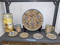 Overview of platter on stand, small dishes, mugs and vase on shelf
