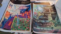Overhead view of two posters laid flat showing abstract design at left and aircraft collage at right