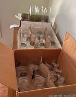 Open cardboard boxes with assorted clear glasses arranged in dividers