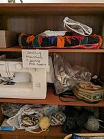Full view of wooden shelving unit with Kenmore sewing machine, skeins of yarn, folded fabric, and miscellaneous supplies.