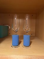 Two Tiffany & Co. champagne flutes placed side by side with blue foam holders at the base inside a wooden cabinet.
