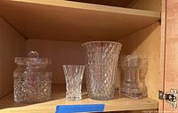Overall photo shows three heavy cut-crystal vases of different patterns and one crystal jar with lid, placed on wooden shelf.