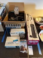 Cardboard box containing Sekonic L-28 meter box, camera strap, Argus flash unit and tripod box visible at right