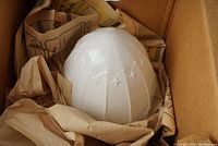 Milk glass pendant lamp globe nestled in packing paper inside cardboard box.