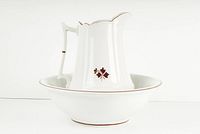 Front side angle of white ironstone wash basin with matching pitcher inside, both decorated with brown tea leaf motif and brown trim.