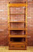 Front view of large tall wooden etagere shelf showing five shelves and bottom drawer with two metal handles against a brick wall background.