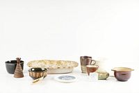 Front view of all pottery items in lot arranged in a row, showing variety of shapes, sizes, and colors.