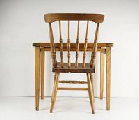 Front view of wooden child's chair showing spindle backrest and rectangular table behind.