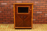 Front view of vintage wooden cabinet showing glass insert on upper door and twin metal handles on lower doors, wood finish with mild wear.