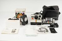 Full lot showing Polaroid OneStep camera, Q-Light flash, Braun flash with box and manual, black camera case, and paperwork.