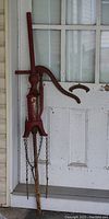 Full front view of vintage red cast iron water hand pump with long handle and chains on base.