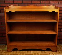 Front view of the wooden bookshelf showing three shelves, a decorative curved apron at the base, and overall finish.