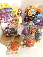 Five vintage McDonald's Halloween character toys still sealed in original clear plastic bags, arranged in front of two different McDonald's Halloween themed cardboard boxes.