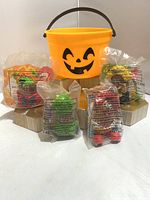 Front view of four sealed 1996 McDonalds Halloween McNuggets figurines in original bags, displayed in front of the 1986 McDonalds Halloween pumpkin bucket with a smiling jack-o'-lantern face and black handle.