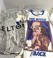 Photo showing the T-shirt laid flat with the tote bag beside it, highlighting the graphic print on the shirt and metallic texture of the bag.