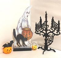 Halloween table decor items including ghost stand, pumpkins, rubber bat, and metal chandelier on a white background