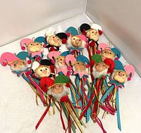 Full view of all twelve handmade holiday elf decorations arranged together showing varied hat colors and ribbon details.