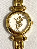 Close-up of watch face showing gold Minnie Mouse figure on white dial with gold markers and round goldtone case.