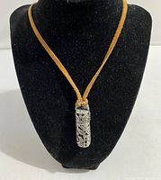 Full view of necklace displayed on black jewelry bust, showing metal pendant with intricate floral design and tan leather strap.