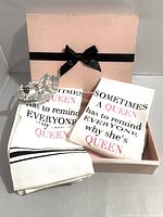 Overall shot of Queen Tea Towels gift set showing the two printed white tea towels, decorative silver crown, and pink gift box tied with black ribbon.