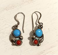 Front view of the pair of sterling silver earrings showing turquoise and red coral stones with detailed silverwork.