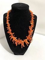 Front angled view of red branch coral necklace on a black display bust, highlighting the irregular coral shapes and vibrant orange color.