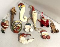 Photo showing 10 different holiday ornaments including Santa Claus figures, a snowman, a reindeer, and a star ornament with Santa face on white background.