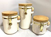 Front view of three ceramic canisters with wood lids and attached scoops in small, medium, and large sizes.
