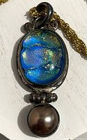 Close-up of the pendant showing oval blue iridescent glass and spherical pearl drop.