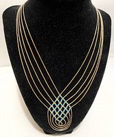 Front view of silver-tone multi-strand necklace with turquoise bead woven centerpiece on black display bust.