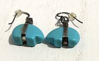 Pair of turquoise carved bear fetish earrings on white surface showing top-down detail, metal hook backs with rubber stoppers in place.