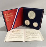 Opened coin holder showing Washington quarter, Kennedy half dollar, and Eisenhower dollar silver proof coins in clear plastic capsules with informational document.